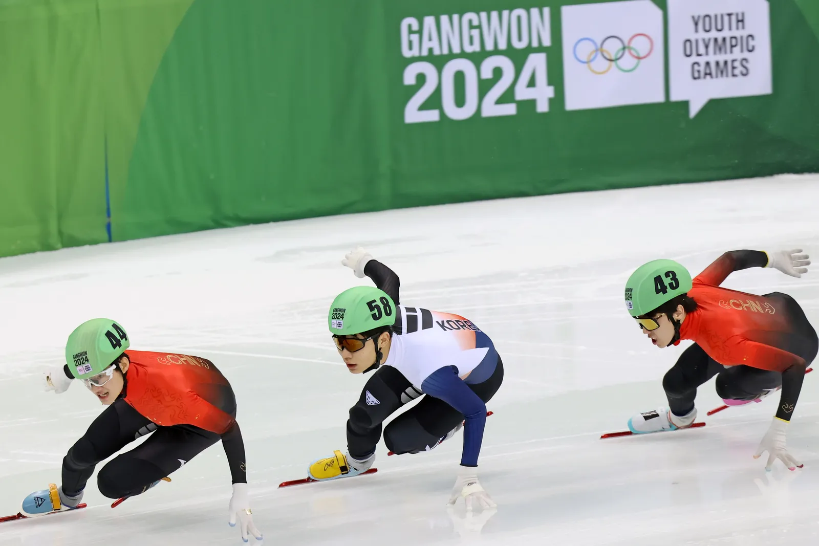 Trois patineurs de short-track penchés dans un virage pendant une course