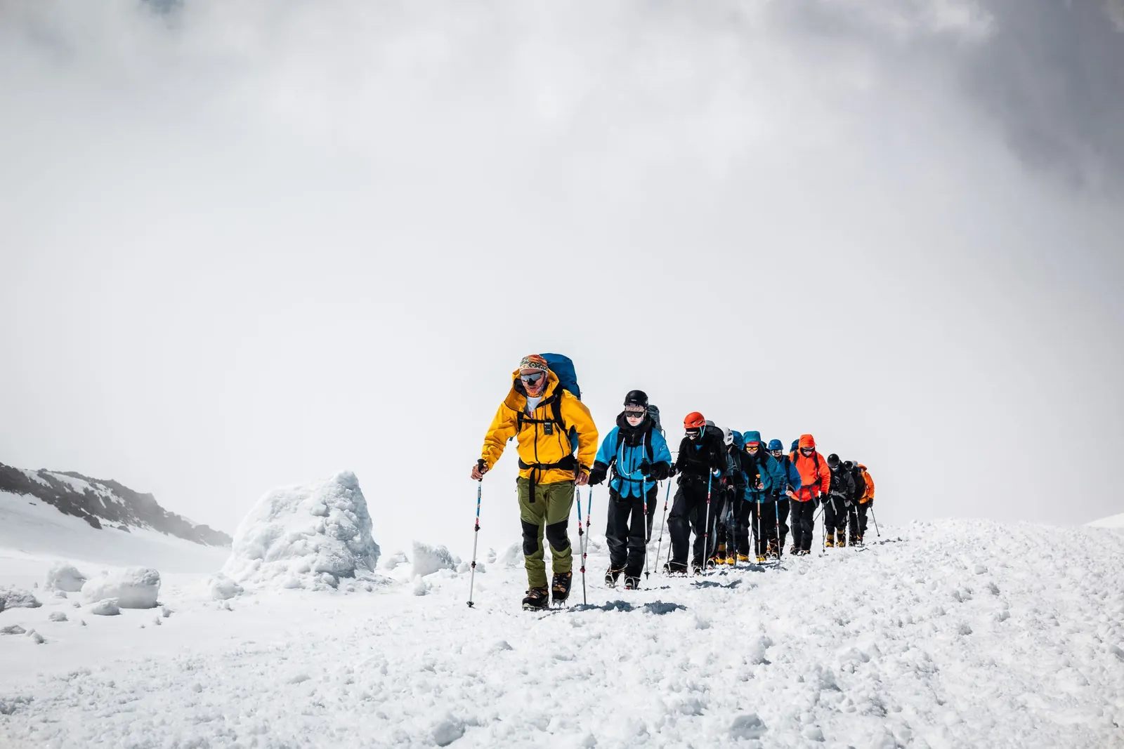 Une cordée d'alpinistes équipés progresse en file sur un glacier enneigé.