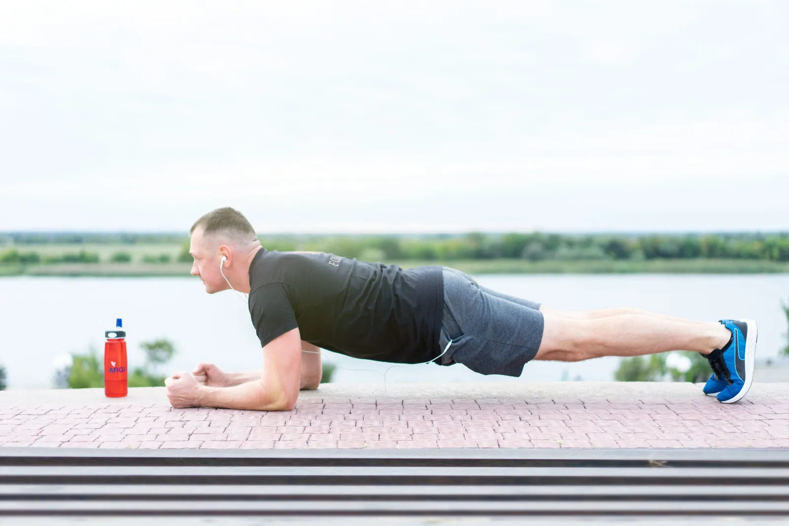 Un homme en tenue de sport fait une planche de gainage abdominal en plein air au bord d'un lac.