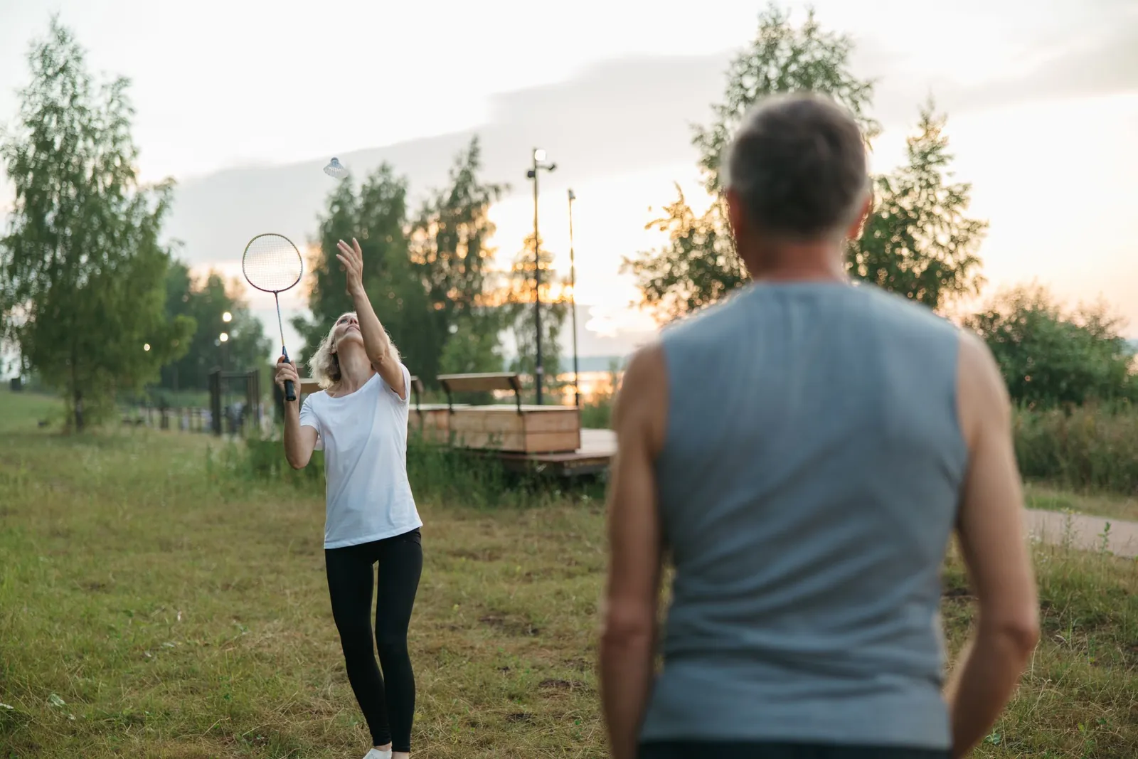 Une femme frappe le volant avec sa raquette lors d'une partie de badminton en plein air face à son partenaire.