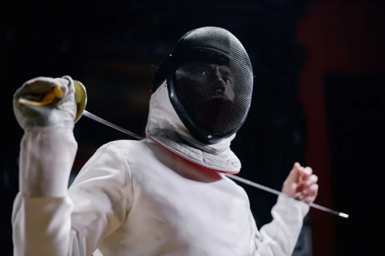 Escrimeur en tenue blanche complète, masque grillagé et épée à la main